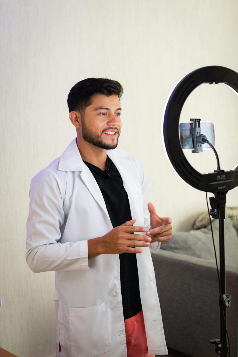Male doctor in a white coat recording video with a ring light, engaging with the audience.